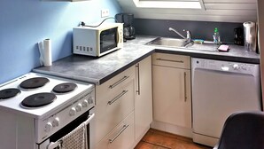 Een kleine keuken met een gasfornuis, magnetron, spoelbak en vaatwasser. Een dakraam zorgt voor natuurlijk licht.