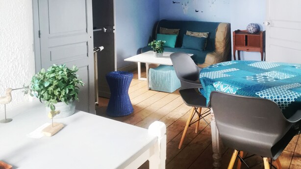 Een kamer met een bed, een tafel, een stoel, een kamerplant en een plafondventilator.