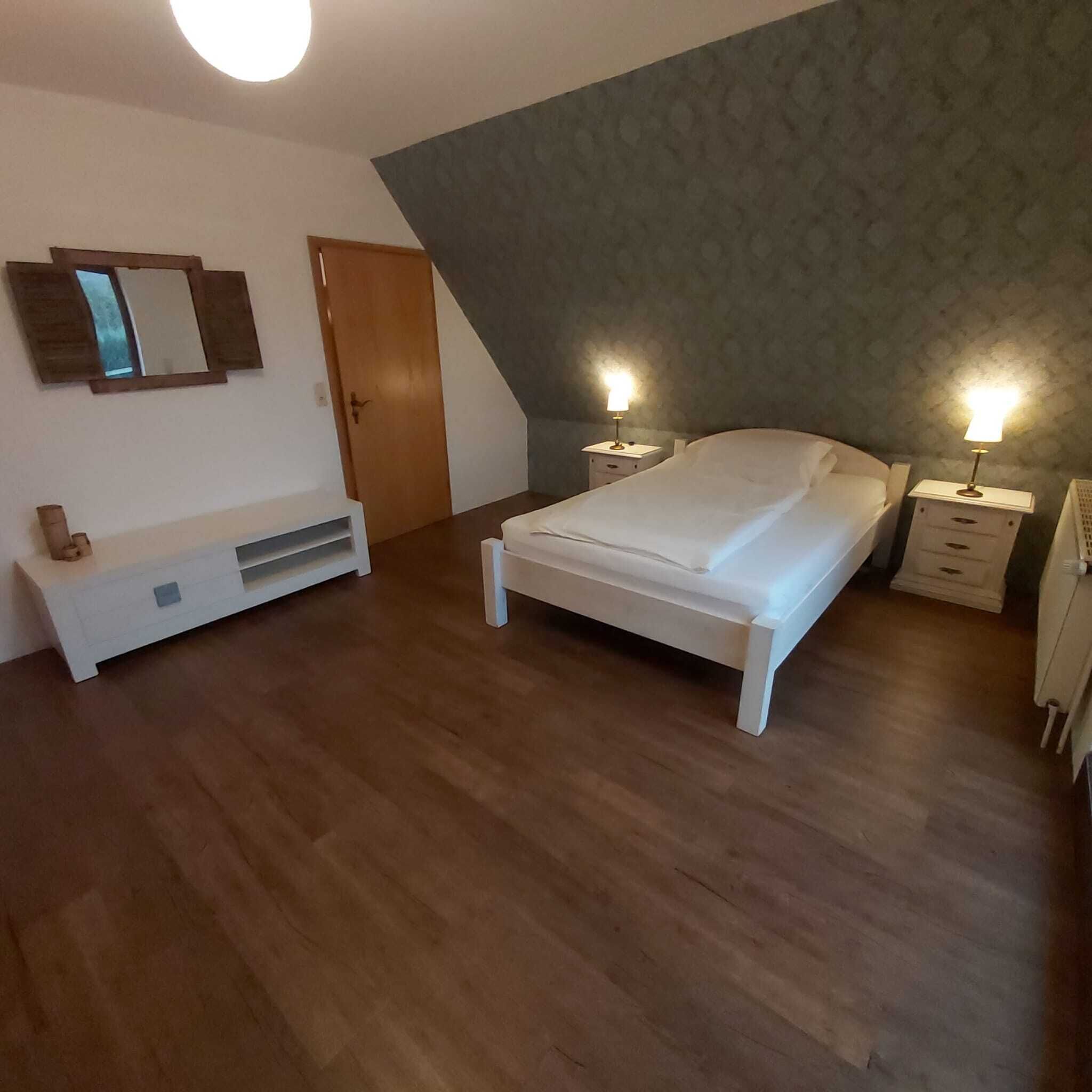 Quarto com cama, mesas de cabeceira, um banco e um guarda-roupa.