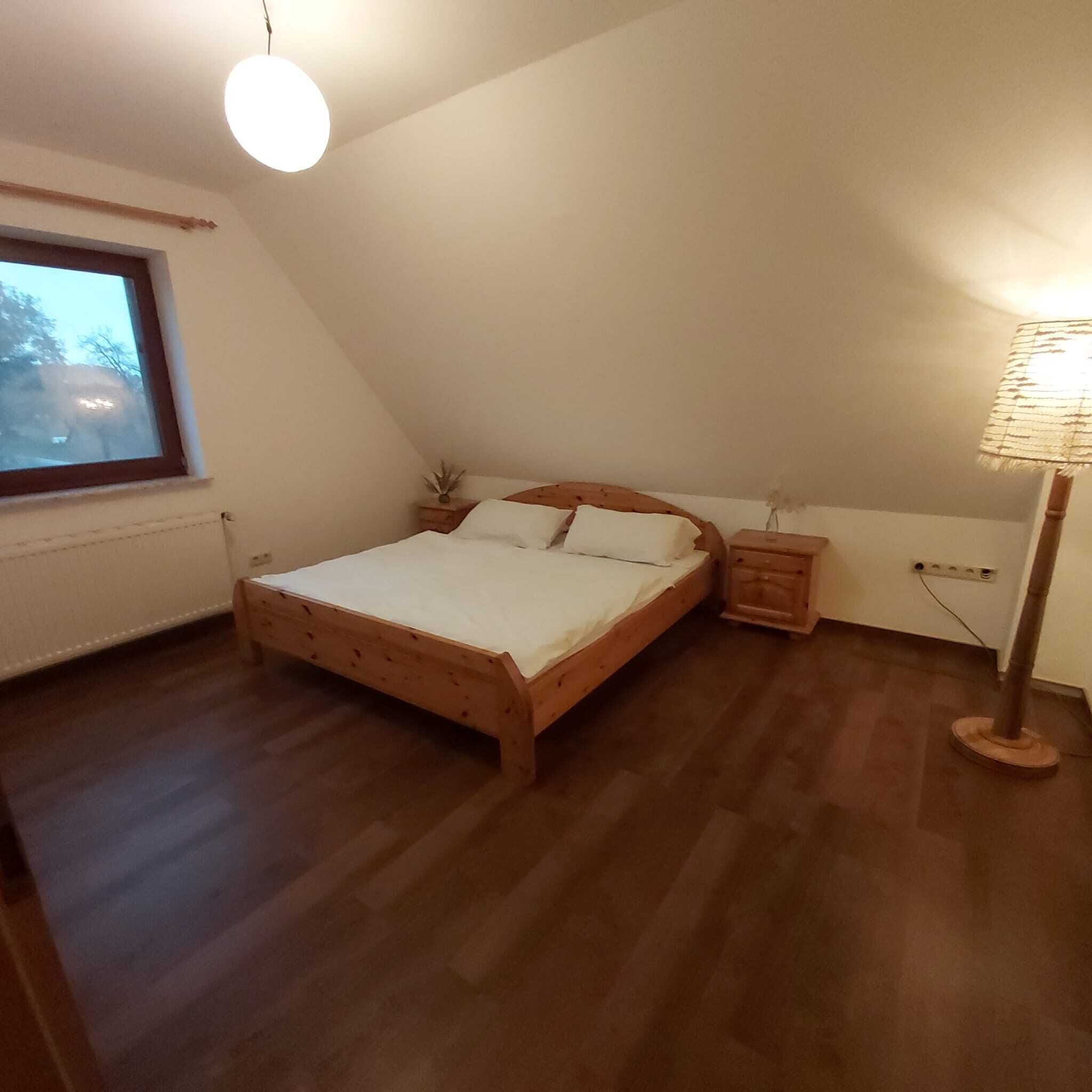 A bedroom with a wooden bed, a nightstand, a lamp, and a window.