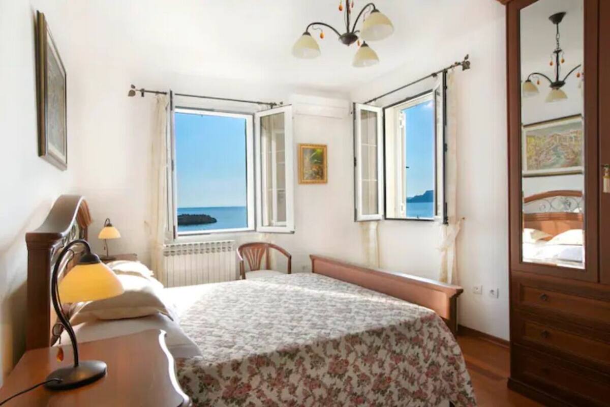 Une chambre à coucher avec un lit, une table de chevet, une lampe, une chaise et une fenêtre donnant sur la mer.