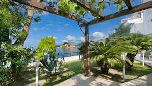A garden with a pergola, palm trees, and a view of a body of water.