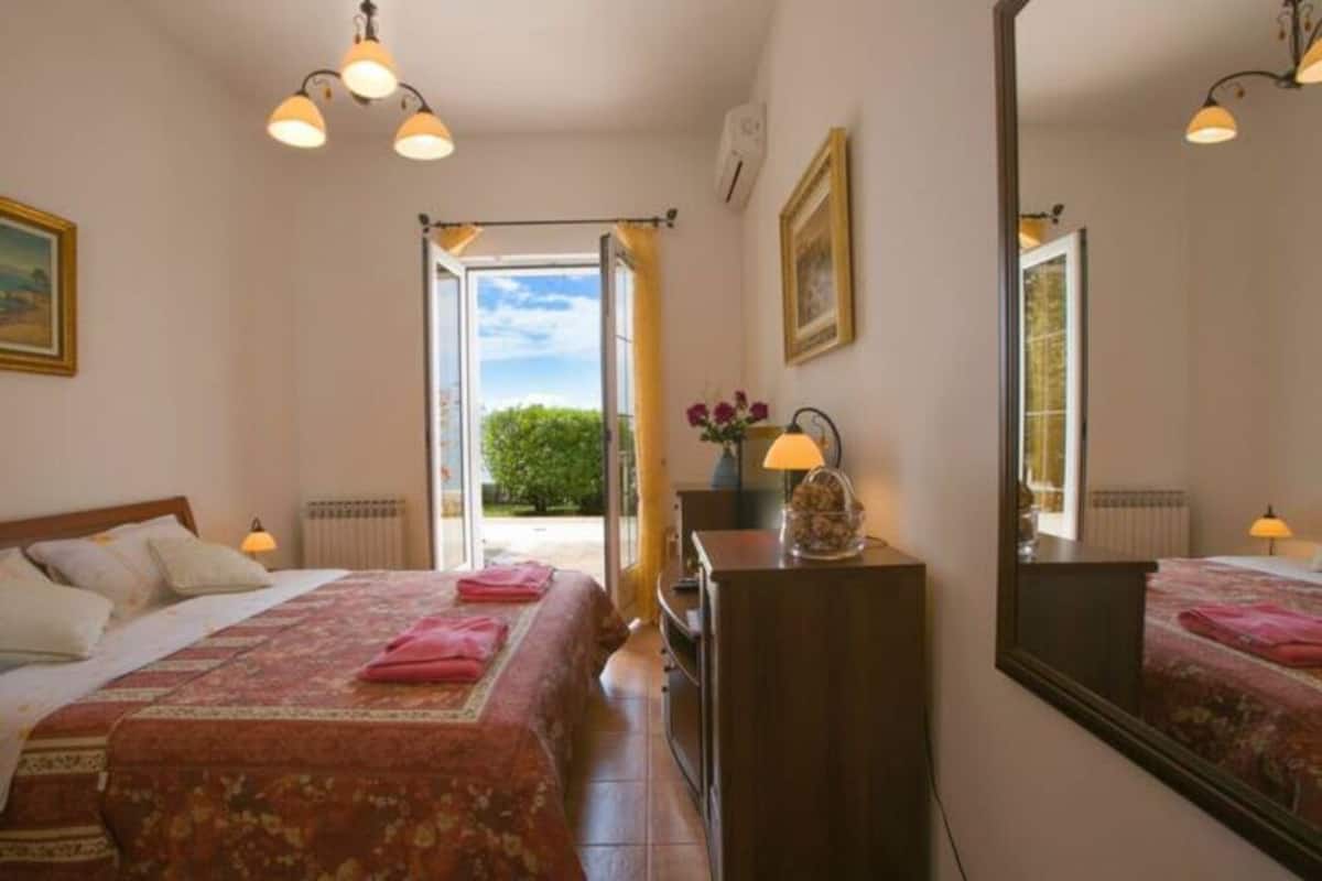 Une chambre à coucher avec un lit, des lampes de chevet, une commode, un miroir et une fenêtre avec des rideaux.