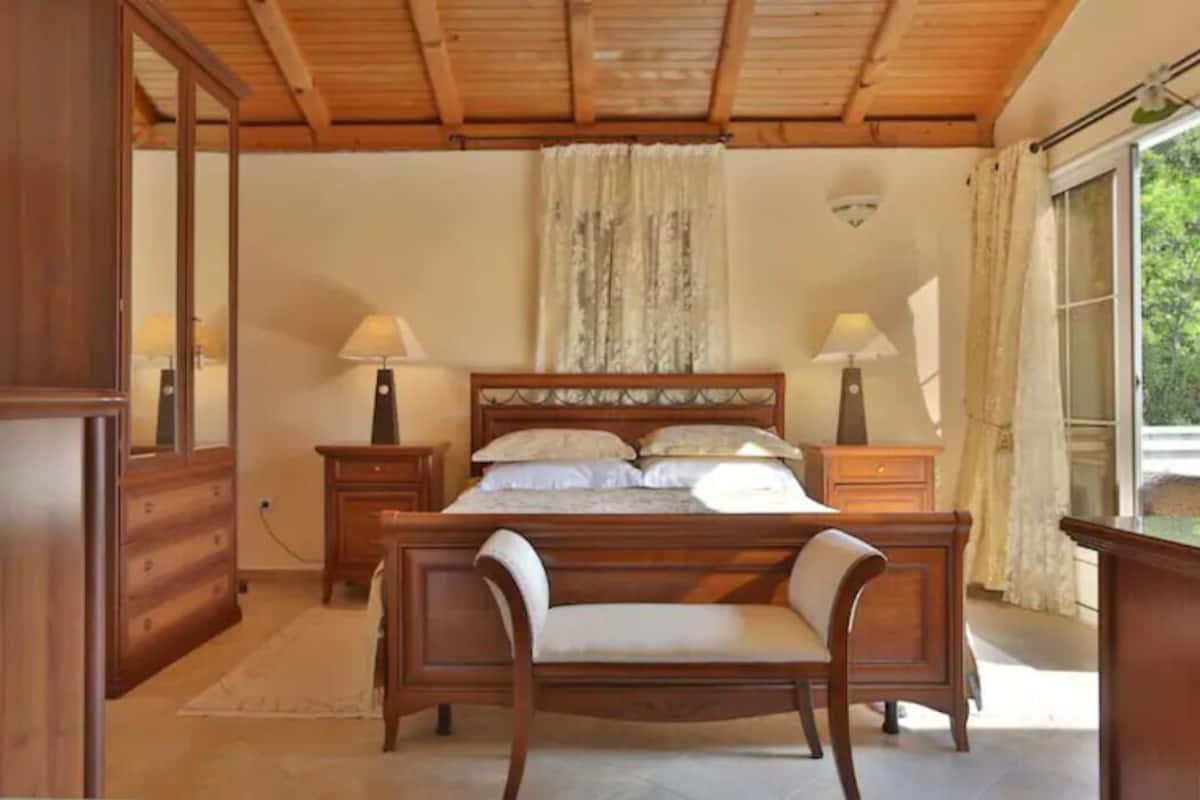 Une chambre à coucher avec un lit en bois, deux tables de chevet avec des lampes, un miroir et une fenêtre avec des rideaux.