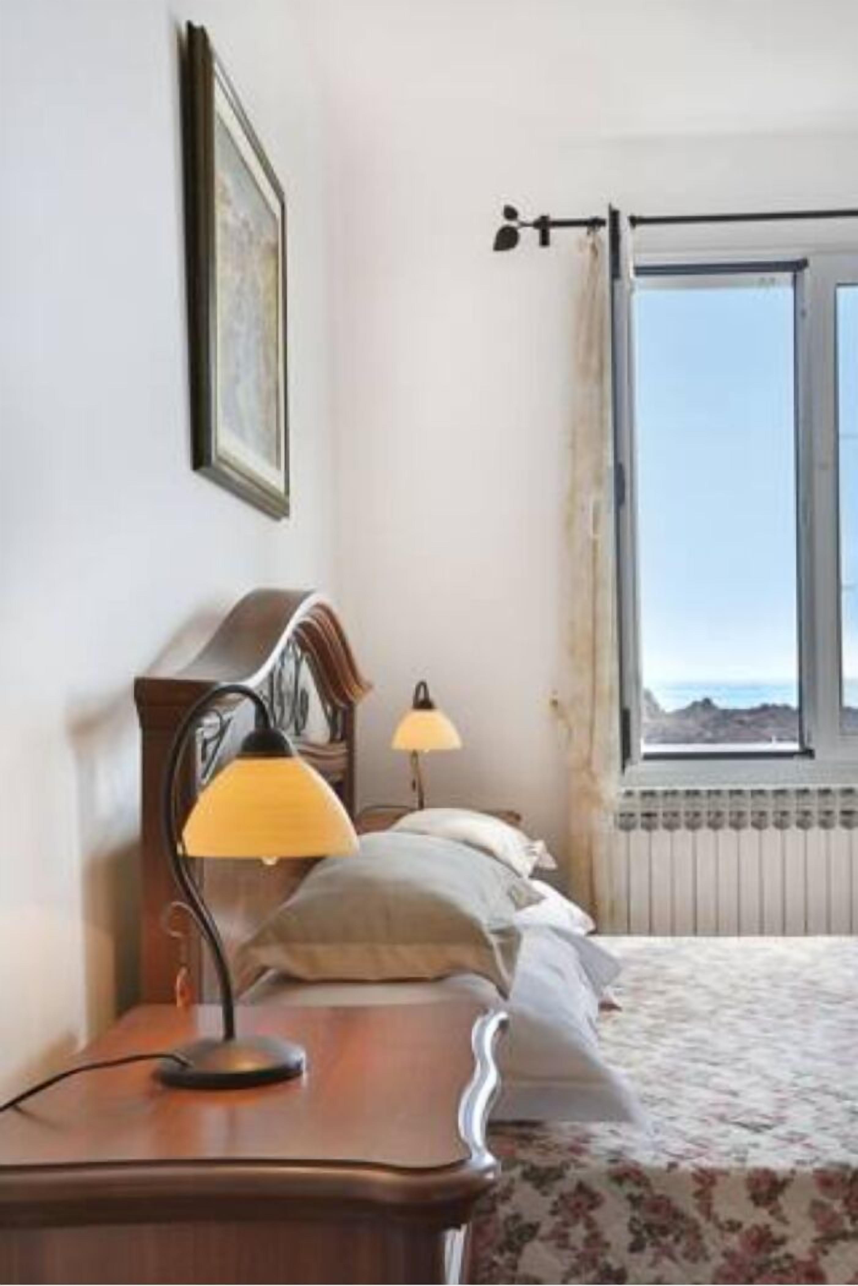 A bedroom with a bed, two bedside lamps, a wooden nightstand, a framed picture on the wall, and a window with a view of the landscape.