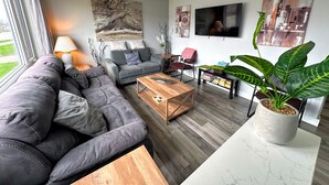 A modern living room with a grey sofa, a wooden coffee table, a flat-screen TV, and a large potted plant.