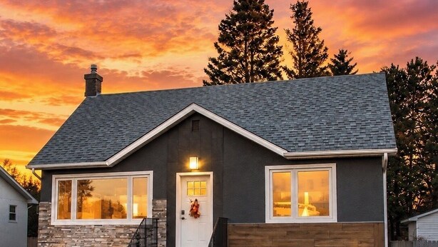 A two-story house with a stone facade, a dark roof, and a front porch with steps.