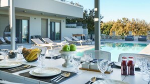 A dining table set outdoors with a view of a swimming pool and lounge chairs.