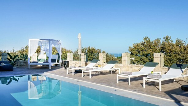 A rooftop pool area with lounge chairs, a canopy, and a view of the sea.
