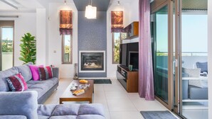 A modern living room with a sofa, coffee table, fireplace, TV, and sliding glass doors to a balcony.