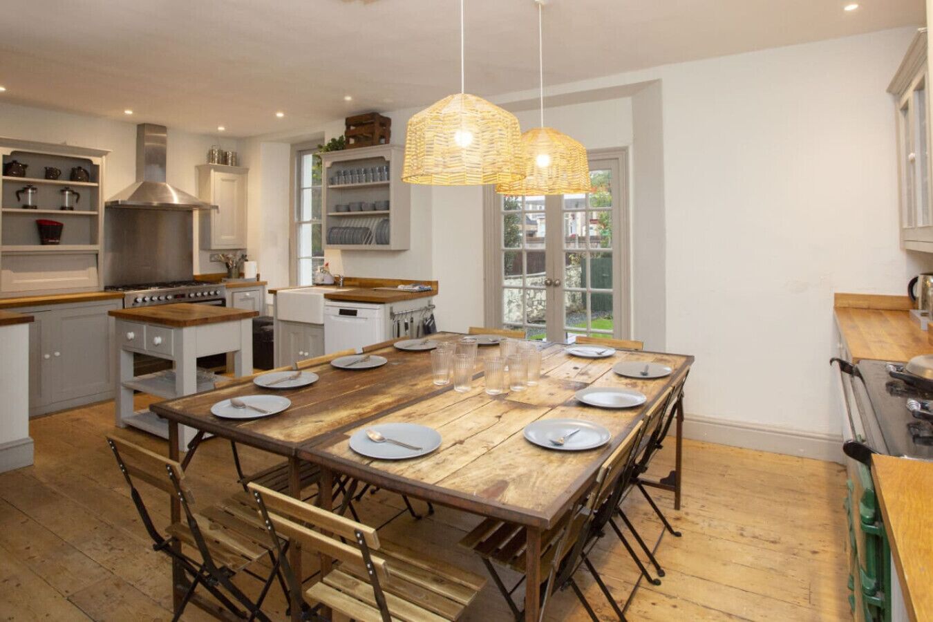 Een ruime keuken met een grote eettafel, houten stoelen en een hanglamp.