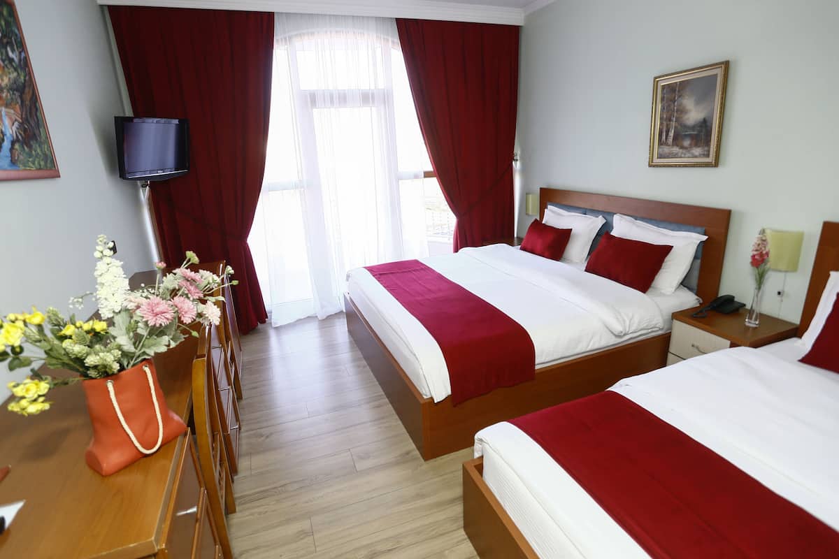 A hotel room with two beds, a TV, a desk with a vase of flowers, and a painting on the wall.