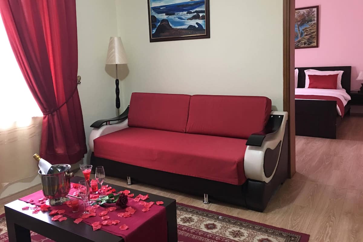 A room with a red sofa, a small table with a bottle and glasses, a lamp, and a painting on the wall.