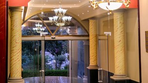 Un vestíbulo con candelabro, columnas de mármol y una entrada de cristal que da a un jardín.