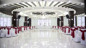 Un salón amplio con suelo pulido, mesas blancas con cintas rojas y un escenario central adornado con arreglos florales.