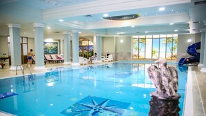 Una piscina interior con diseño de estrella de mar en el suelo, rodeada de sillones de descanso y vistas a palmeras a través de amplias ventanas.