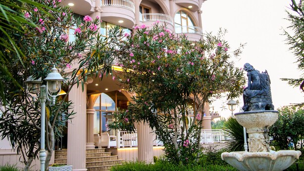 Un edificio de varios pisos con balcones, una fuente y mesas al aire libre.