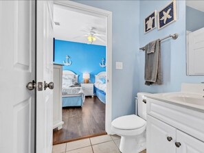 Ein Schlafzimmer mit blauer Akzentwand, einem weißen Deckenventilator, einem Bett mit weißer Bettwäsche und einem Nachttisch mit Lampe.
