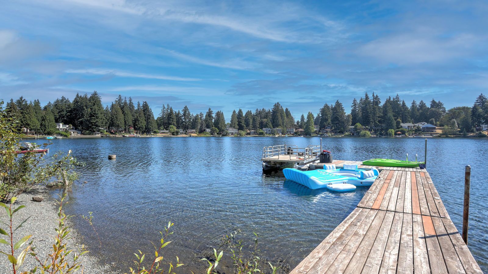 A wooden dock extending into calm water with a rowboat and inflatable floatation devices docked.