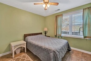 A bedroom with a bed, a nightstand, a lamp, a ceiling fan, and a window with curtains. - HOT TUB, FIRE PIT, PET FRIENDLY! Visit LONGHAVEN! (Huddleston)