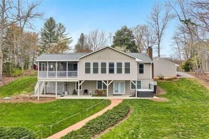 A two-story house with a covered porch, a small deck, and a front yard with a pathway. - HOT TUB, FIRE PIT, PET FRIENDLY! Visit LONGHAVEN! (Huddleston)