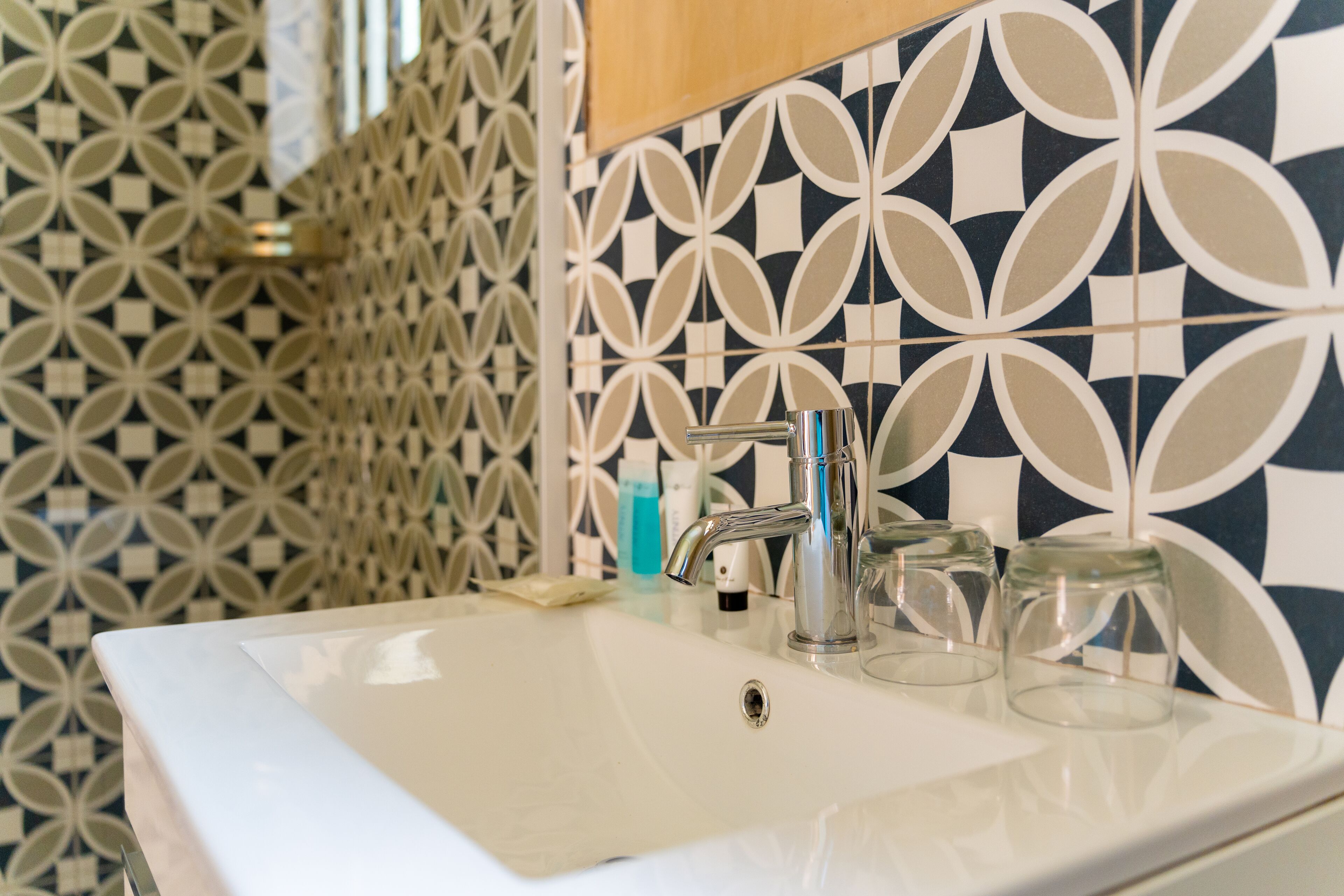 A bathroom with a white sink, a modern faucet, and patterned tiles on the walls.