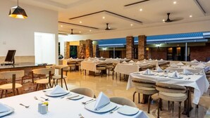 A spacious dining area with multiple tables set for service, a bar area, and a view of the outside. - The Shrub lodge (Victoria Falls)