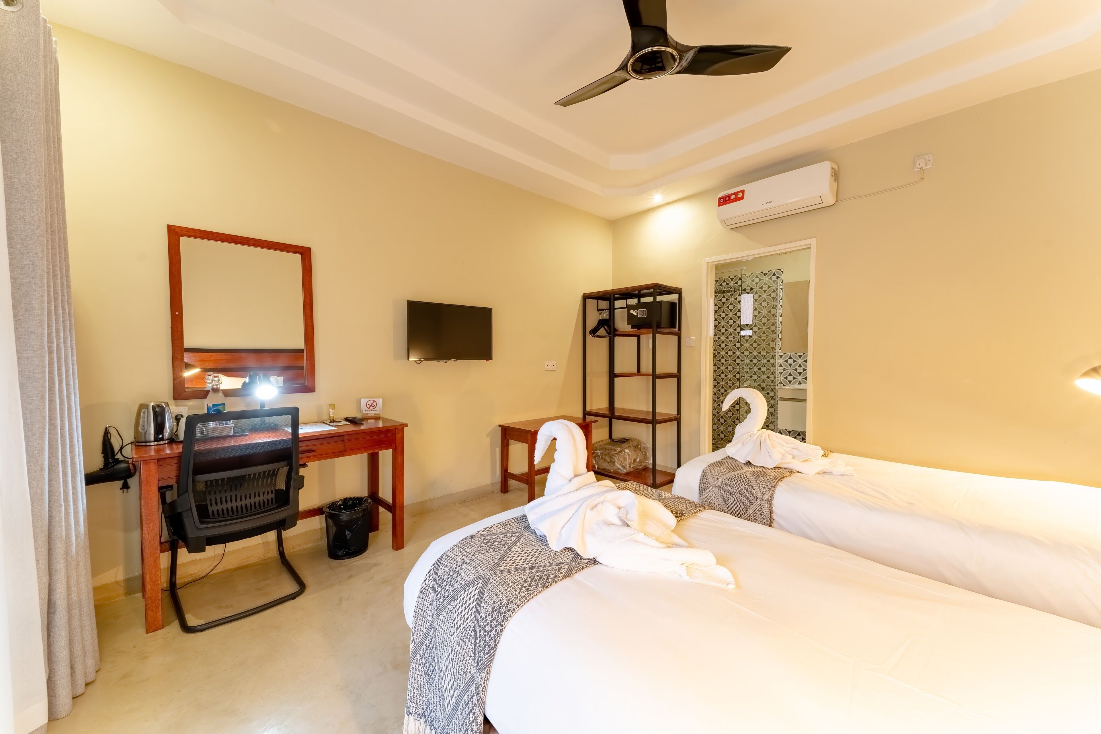 A hotel room with two beds, a desk with a chair, a TV, and a ceiling fan.