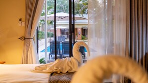 A hotel room with a bed, a window with curtains, and a view of an outdoor pool area. - The Shrub lodge (Victoria Falls)