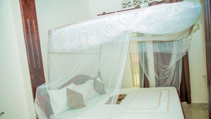A bed with a canopy, a bedside table, and a window with curtains. -  LEISURE INN (Muhoza)