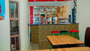 A bar area with a counter, stools, and shelves stocked with bottles. -  LEISURE INN (Muhoza)