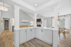 A modern kitchen with white cabinetry, a wooden floor, and a dining area with a table and chairs.