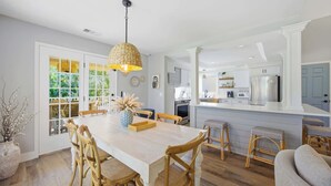 Een ruime keuken met witte kasten, een centraal eiland en een eethoek met houten stoelen en een tafel.