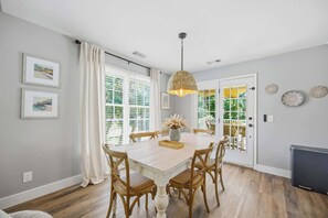A dining area with a table, chairs, a hanging light fixture, and a door with a view.