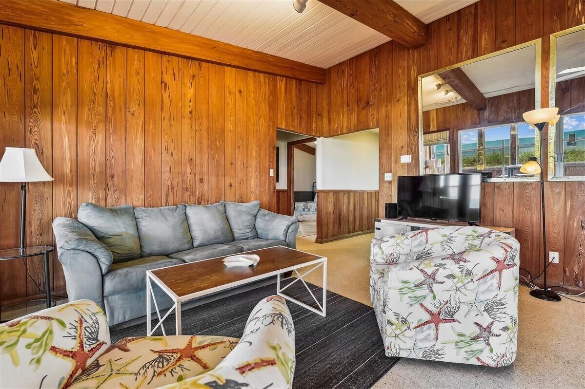 A cozy living room with a wooden wall, a grey sofa, a wooden coffee table, and a patterned armchair.
