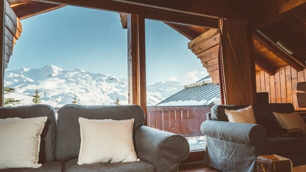 Una habitación acogedora con un ventanal grande que ofrece vistas de montañas nevadas.