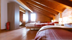 Un dormitorio cálido en el ático con techo de madera, una cama grande con ropa de cama roja, una mesita de noche con una lámpara y vistas a un baño a través de una puerta abierta.