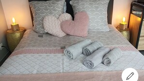 Un lit bien fait, avec une literie à motifs, des oreillers en forme de cœur et des serviettes enroulées.