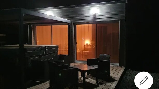 Un espace extérieur aménagé en terrasse, avec une plateforme en bois, du mobilier d’extérieur noir et une grande porte-fenêtre coulissante donnant sur un espace intérieur.
