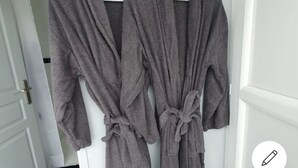 Deux robes grises, nouées à la taille, sont accrochées à une porte blanche.