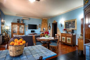 Ein Essbereich mit Tisch, Stühlen, einer Korb voller Orangen und einem Fernseher.