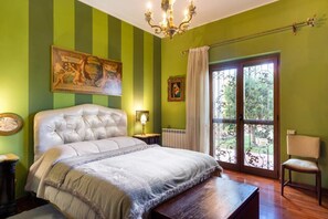 Ein Schlafzimmer mit einer gesteppten Kopfteil, einem großen Bett, einer Kristallleuchtre, einem Fenster mit Aussicht und einem Gemälde an der Wand.