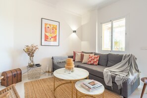 Un salon comprenant un canapé, une table basse, une table d’appoint, un vase avec des fleurs séchées, un tableau encadré et une fenêtre donnant sur un beau paysage.