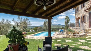 Un espacio al aire libre techado con piscina, mobiliario y vistas al campo.