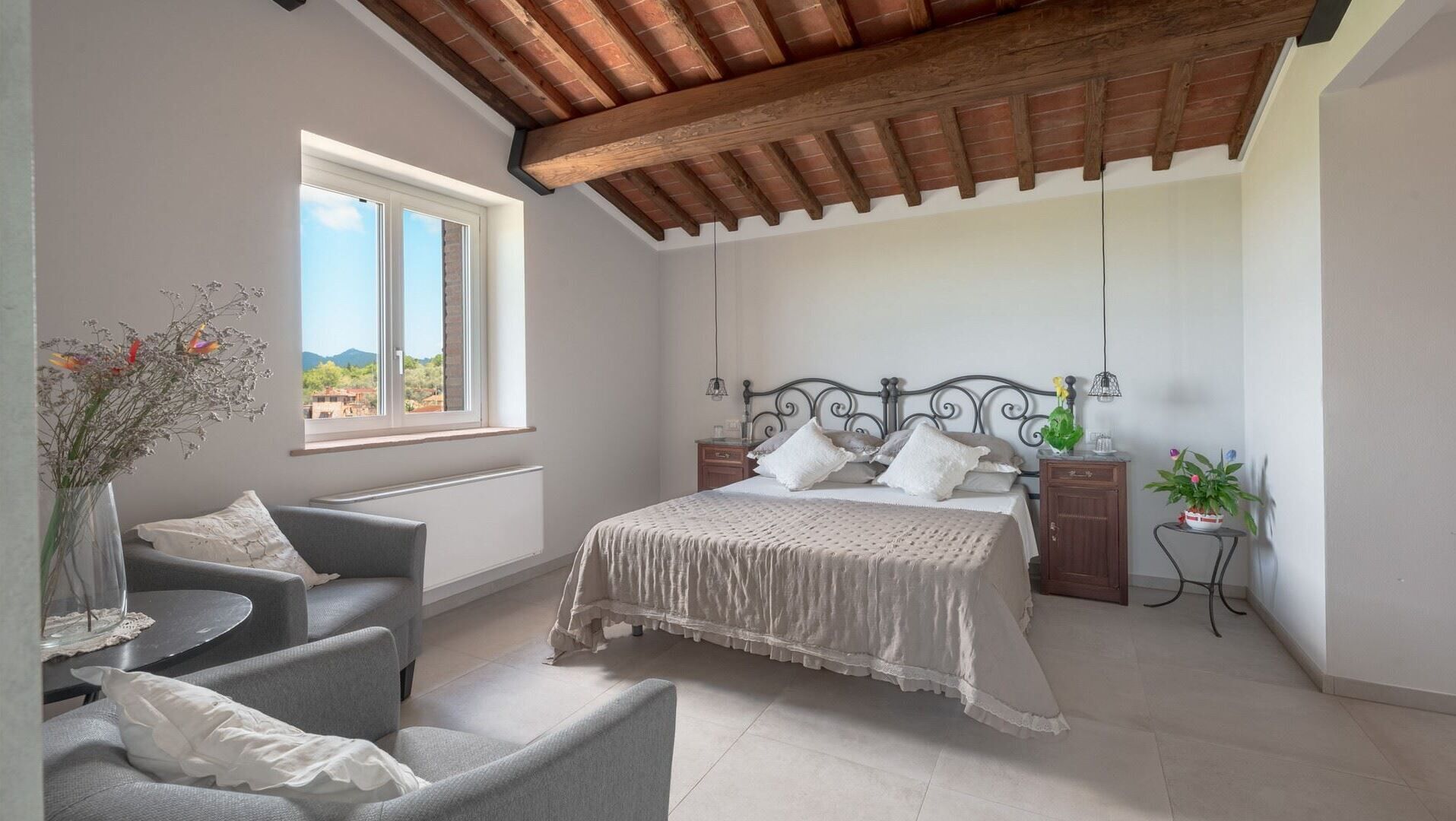 A bedroom with a bed, a chair, a nightstand, a potted plant, and a window with a view.