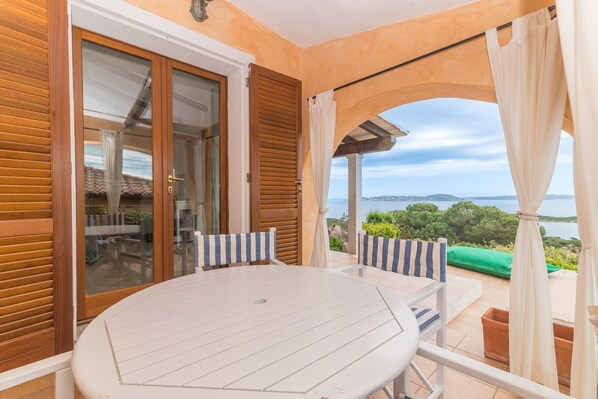 A balcony with a white table and chairs, a view of the sea, and a wooden door.