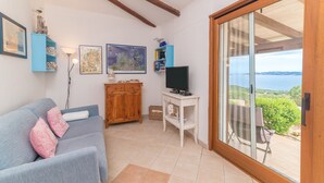 Un soggiorno con divano, televisione, mobiletto in legno e vista panoramica tramite una porta scorrevole in vetro.