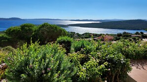 Vista sulla costa da una zona esterna riparata, con cielo sereno, un corpo d'acqua e colline in lontananza.