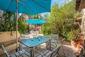 A patio with metal tables and chairs, a blue umbrella, and potted plants.