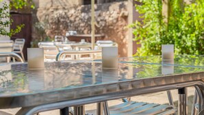 A glass-top table with metal chairs, a stone wall, and greenery in the background. - Apartment "Segles 11" with Shared Pool & Wi-Fi (Campos)